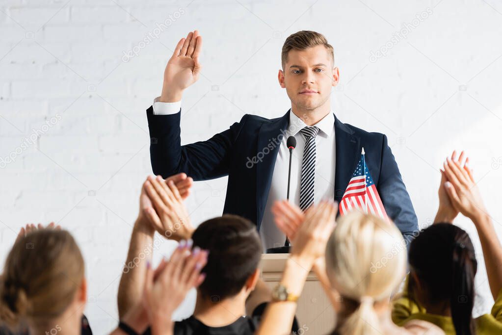 confident candidate showing swear gesture in front of applauding voters in conference room