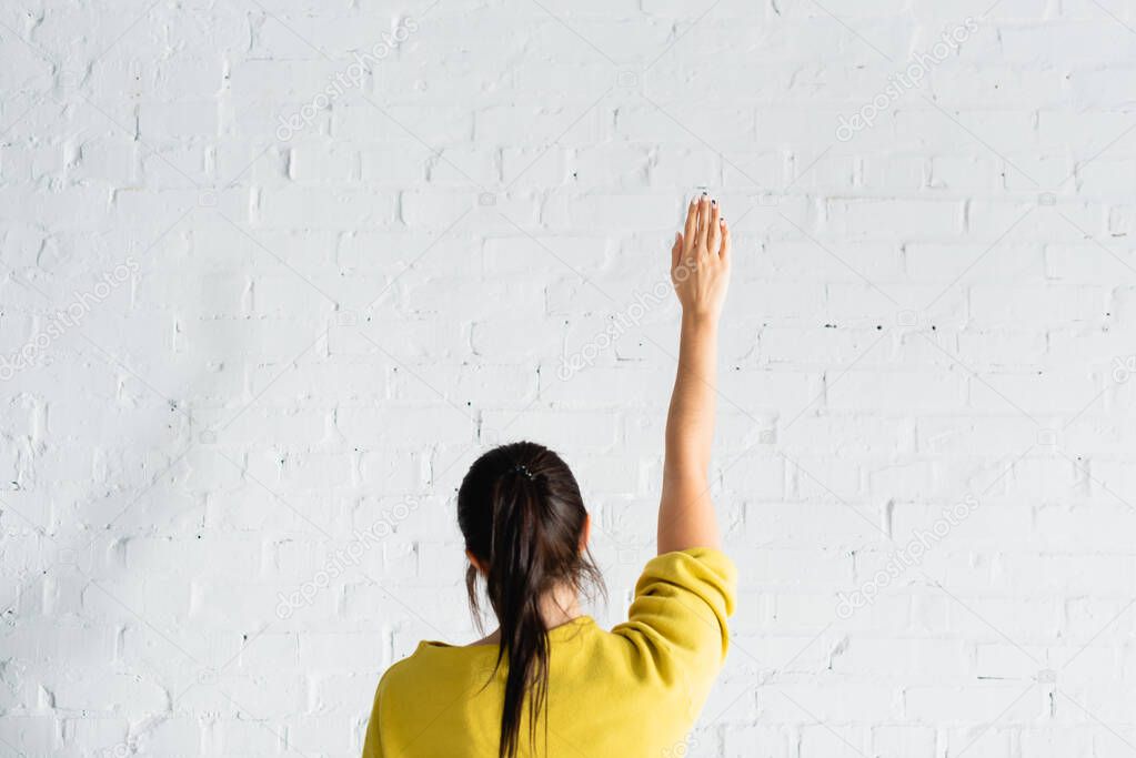 back view of woman voting with hand in air against white brick wall