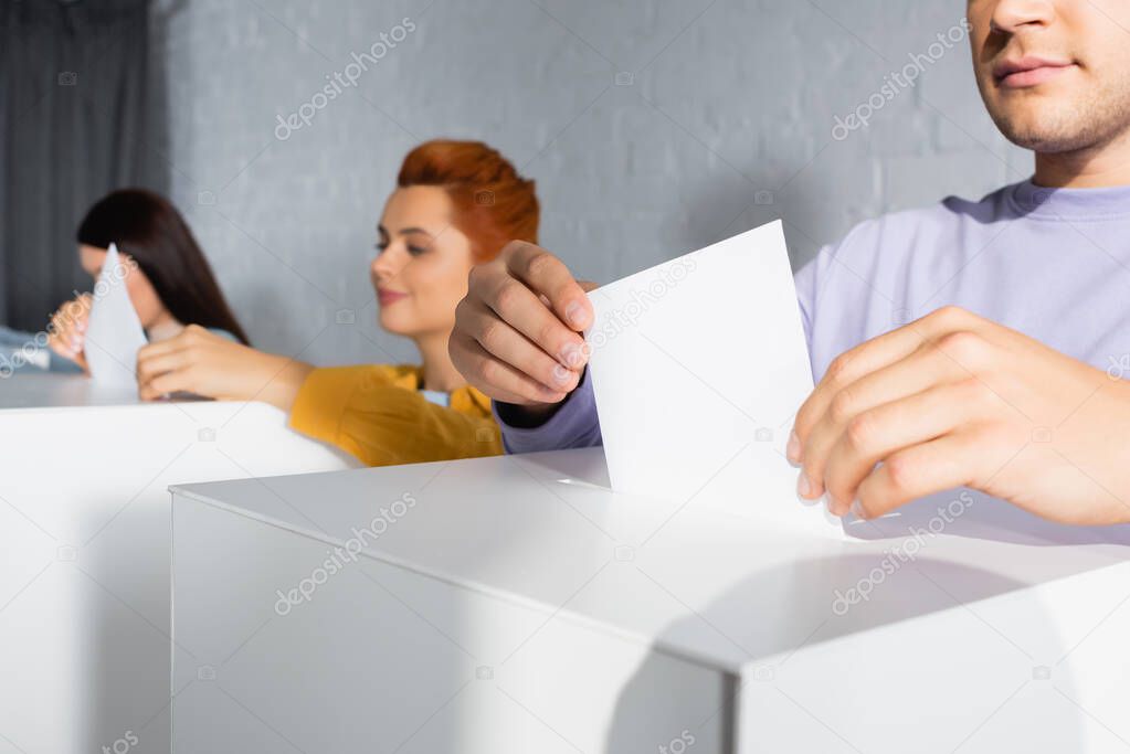 electors inserting ballots into polling boxes on blurred background