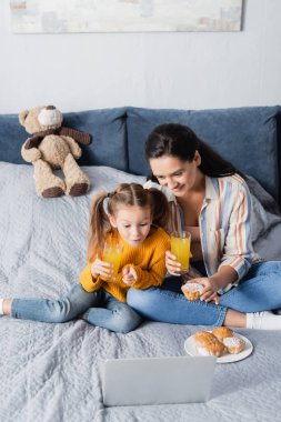 Gülümseyen bir kadın ve heyecanlı bir kızın dizüstü bilgisayardan kek ve portakal suyuyla film izlemesi.