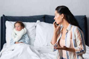 Endişeli bir kadın cep telefonuyla konuşurken geçmişi bulanık hasta bir kızın yanında el kol hareketi yapıyor.