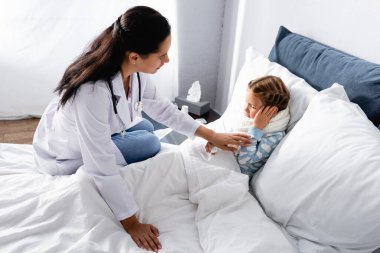 Doktor yatakta yatarken kulak ağrısı çeken çocuğa dokunuyor.