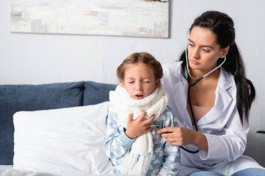Yatak odasında steteskopla öksüren çocuğu muayene eden çocuk doktoru.