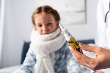 Burun spreyi tutan doktor bulanık arka planda hasta kızın yanında.