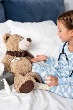 girl curing teddy bear while playing in bed clipart