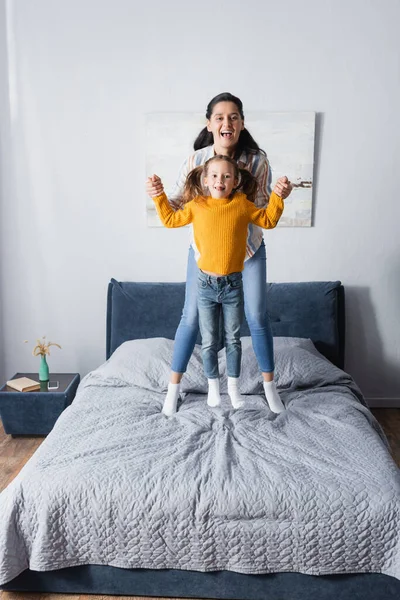 Alegre Madre Hija Cogidas Mano Mientras Saltan Cama —  Fotos de Stock