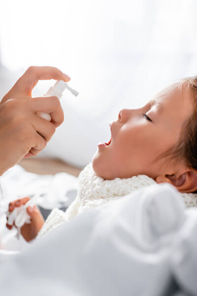 вид сбоку матери, наносящей спрей на больное горло больной дочери