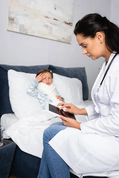 Niña Enferma Tocando Frente Mientras Médico Usa Tableta Digital — Foto de Stock