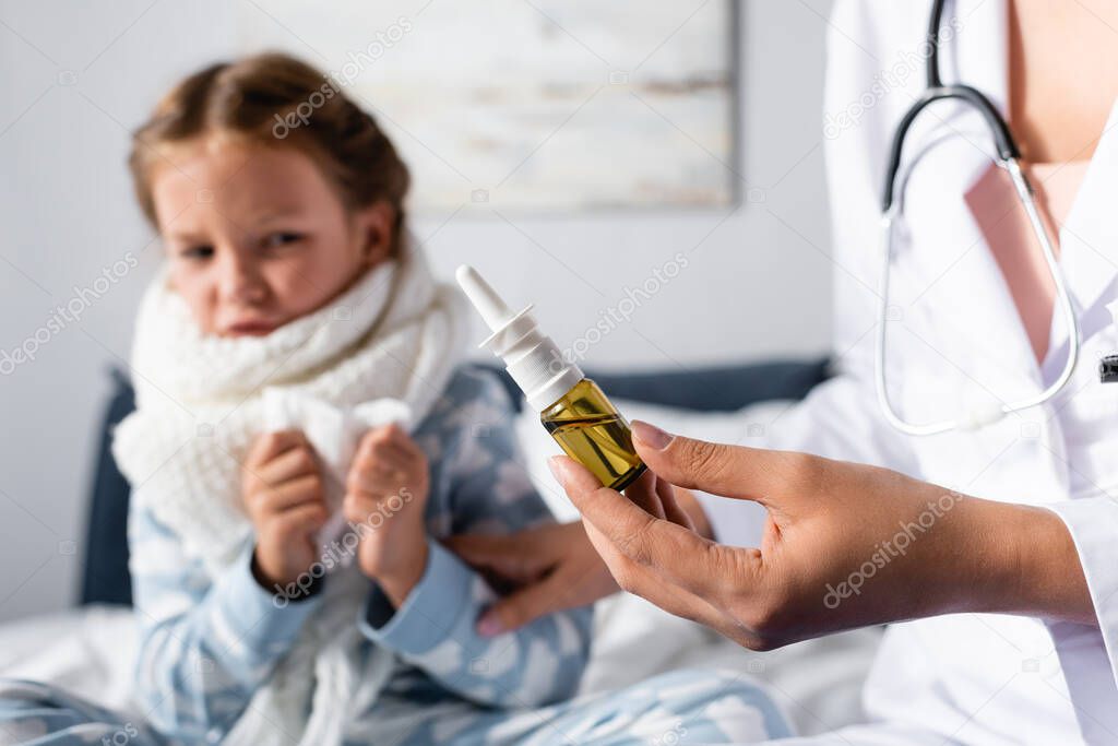 pediatrician holding nasal spray near sick, scared kid on blurred background