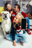 šťastná dívka drží smartphone s prázdnou obrazovkou a rozmazané rodiny na pozadí