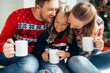 Mutlu bir aile süveter içinde, ellerinde bardaklarla Noel 'de içki tutuyor. 
