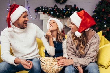 Noel Baba şapkalı mutlu ebeveynler kızlarının patlamış mısır yemesine bakıyor. 
