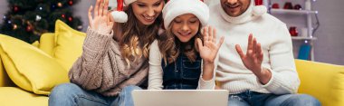 Noel Baba şapkalı neşeli bir aile Noel 'de görüntülü sohbet ederken el sallıyor.