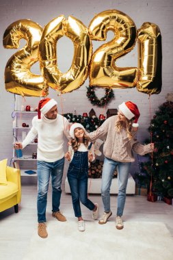 Noel Baba şapkalı mutlu aile hediyelerin yanında duruyor ve üzerinde 2021 numara olan parlak balonlar. 