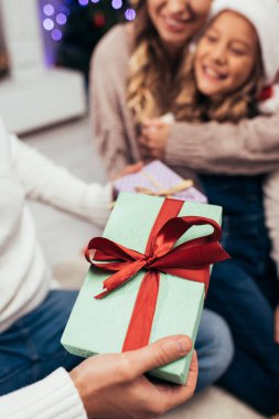 Arka planda bulanık bir ailesi olan bir adamın ellerinde Noel hediyesi.