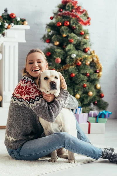 Szczęśliwa Kobieta Zamkniętymi Oczami Siedzi Podłodze Przytula Labrador Pobliżu Choinki — Zdjęcie stockowe