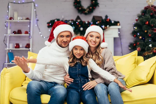 joyful family in santa hats looking at camera in decorated living room