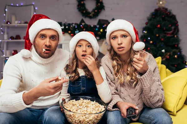 Überraschte Familie Weihnachtsmannmützen Blickt Die Kamera Und Isst Popcorn — Stockfoto