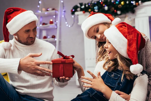 Vater Weihnachtsmannhut Überreicht Geschenk Glückliche Tochter Nahe Ehefrau — Stockfoto