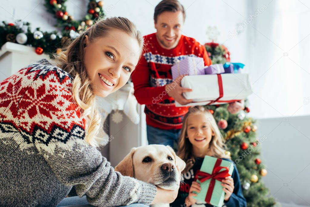 selective focus of happy woman cuddling dog near daughter and husband with gifts on christmas 