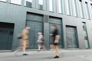 motion blur of people walking on modern street near grey building  clipart