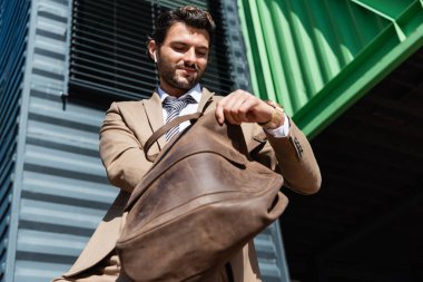 Deri çantalı, kablosuz kulaklıklı mutlu iş adamının düşük açılı görüntüsü 