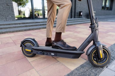 E-scooter ve binanın yanında dururken deri çanta tutan işadamının kısmi görüntüsü 