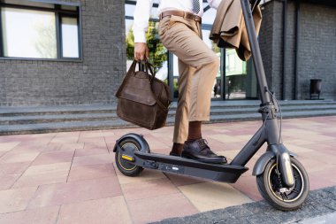 E- scooter 'ın yanında deri çantalı, resmi giyinmiş işadamı manzarası 