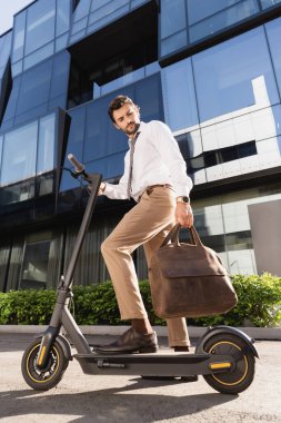 Deri çantalı, elektrikli scooter kullanan resmi giysili sakallı bir iş adamı. 
