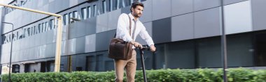 Resmi kıyafetli sakallı işadamı elektrikli scooter ve pankart kullanıyor.