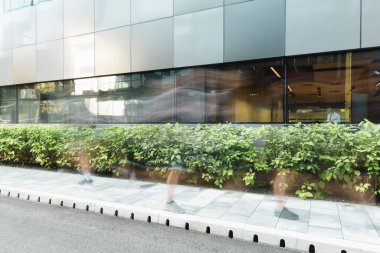 motion blur of people walking on urban street near modern building and plants clipart