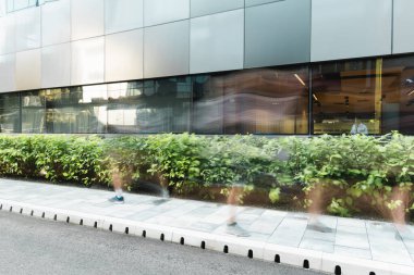 motion blur of people walking on urban street near modern building and green plants clipart