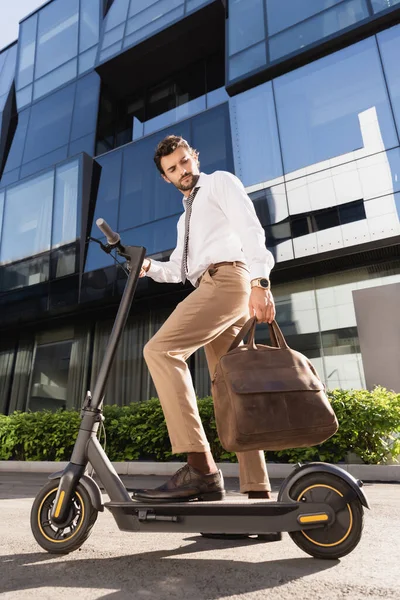 Deri çantalı, elektrikli scooter kullanan resmi giysili sakallı bir iş adamı. 