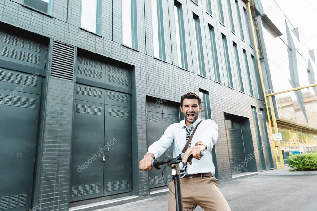 amazed businessman in suit riding electric scooter near building 