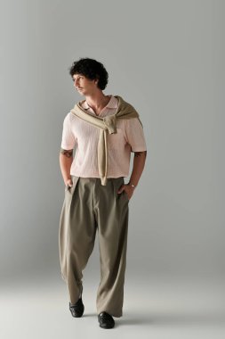 Şık genç adam kendine güvenerek yürüyor, eşsiz bir örgü bluz ve geniş pantolon giyiyor..