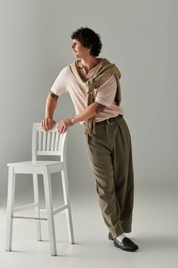 Yakışıklı genç adam şık bir çevrede sandalyeye yaslanırken şık bir kıyafet sergiliyor..