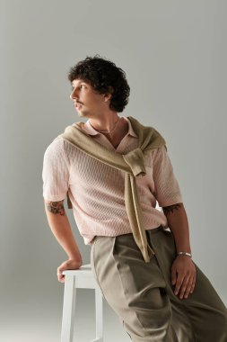 Yakışıklı genç bir adam zarif bir şekilde sandalyede poz veriyor, şık kıyafetlerini yumuşak renklerle sergiliyor..