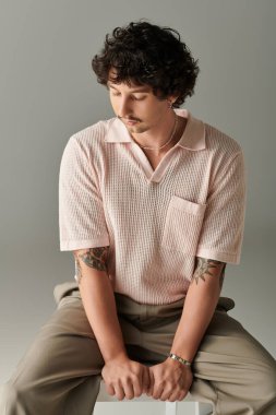 Şık giyinmiş kendine güvenen genç bir adam minimalist bir stüdyoda poz veriyor, karizma ve yetenek saçıyor..