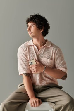 Sıradan giyinmiş yakışıklı genç adam elinde akıllı bir telefonla moda anlayışını sergiliyor..