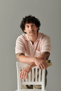 Moda kıyafeti giyen yakışıklı genç adam beyaz bir sandalyeye yaslanıyor, karizma ve tarz yayıyor..