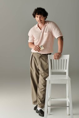 Yakışıklı genç bir adam, beyaz bir sandalyenin yanında dururken modern moda sergiliyor..