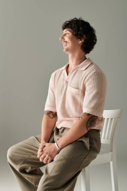 Şık genç adam kendine güvenen bir şekilde sandalyede poz veriyor, şık kıyafetlerini ve karizmasını sergiliyor..