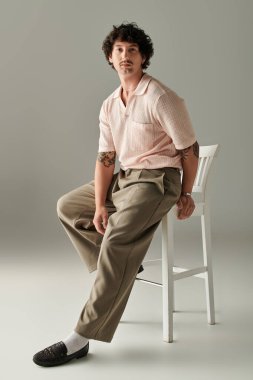 Yakışıklı genç bir adam minimalist bir sandalyeye oturmuş modern moda seçimleri sergiliyor..