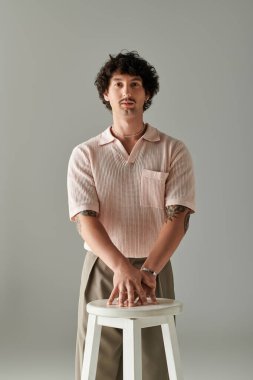 Yakışıklı genç adam kendine güveni olan bir taburede poz veriyor, çağdaş moda ve tarzı sergiliyor..