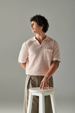 Yakışıklı genç adam, modern moda ve zarafeti sergileyen bir taburenin yanında güvenle duruyor..