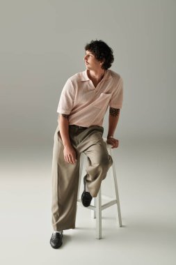 Tarz bir tonda, modaya uygun giyinmiş şık bir genç adam bir taburede oturuyor..