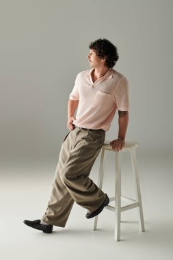 Yakışıklı genç adam şık giyinmiş, cazibeli bir şekilde tabureye yaslanıyor..