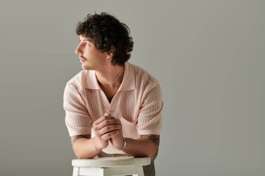 Yakışıklı genç adam bir taburede oturur, modaya uygun giyinmiş bir şekilde derin bir tefekkür eder..