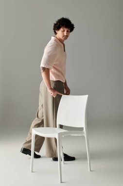 Şık giyinmiş genç bir adam modern bir stüdyo ortamında bir sandalyeyi hareket ettiriyor..