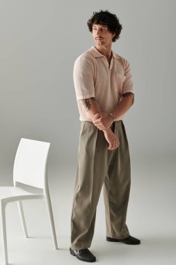 Şık giyinmiş yakışıklı genç bir adam zarif bir şekilde bir sandalyenin yanında duruyor..